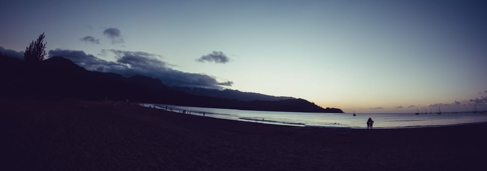 A couple enjoying the sunset with little boats in the background in Hanalei bay, Kauai.
