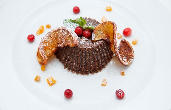 Chocolate orange cupcake decorated with fresh berries, sliced orange, mint on white plate