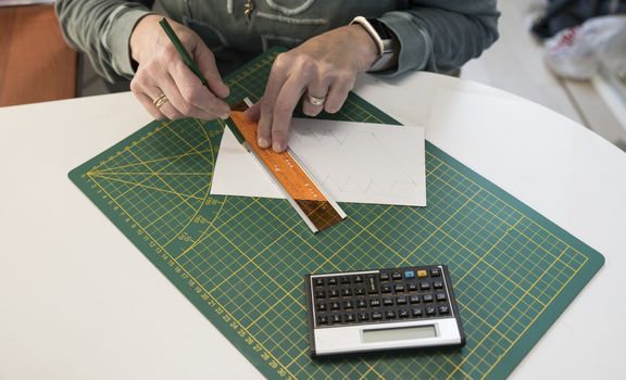woman busy on a desk with calculating and drawing special designs from paper with green pencil and on a white desk