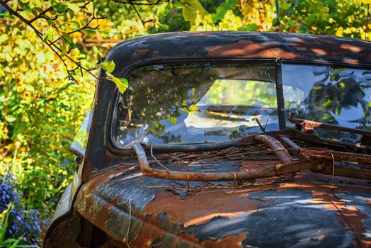 An old retro car. An old rusty retro car stands on a street on a summer day under green trees.