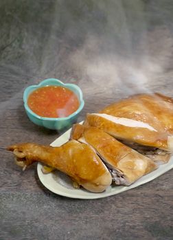 Steamed chicken with soy sauce on dish served with chili sauce in green bowl , Asian style food