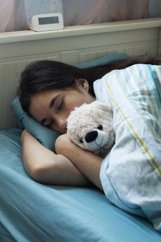 The young girl has a cold, lies in bed at home, feels unwell, takes medicines and vitamins, sleeps with a toy bear.