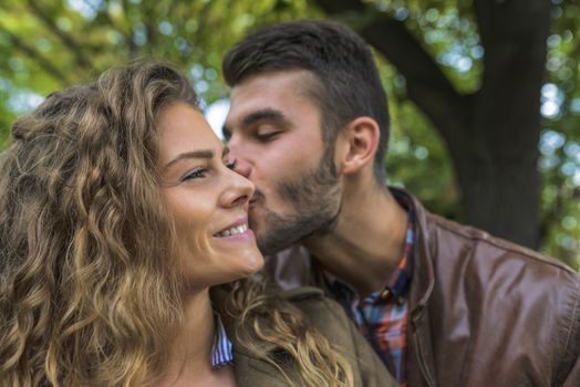 Modern guy with beard kissing his girlfriend in the public park