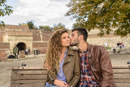 Modern guy with beard kissing his girlfriend in the public park