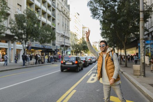 Handsome hipster with orange jacket and sunglasses stopping taxi in the city street