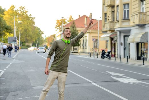 Young man with green headphones stopping taxi in the city street