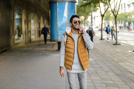 Young hipster with orange jacket and sunglasses with his smart phone in the city street