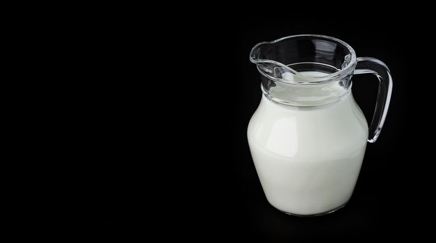 Glass jug of fresh milk on black background with copy space, pitcher of cream