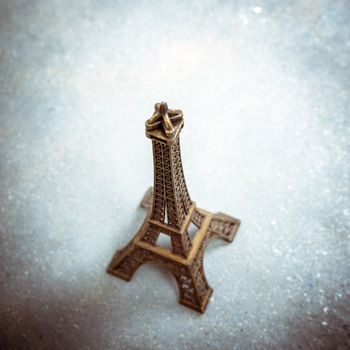 Souvenir model of the Eiffel Tower on cement floor. Strong vignette, split toning effect and film grain filters.