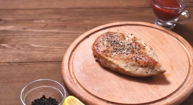 Grilled chicken fillet in spices, next to a saucer, spices and lemon, side view