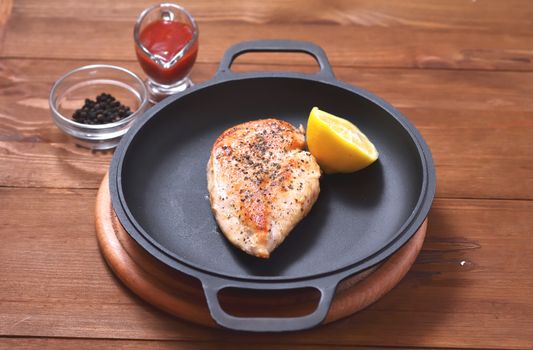 On a frying pan is a fried chicken breast with lemon, spices and a saucepan