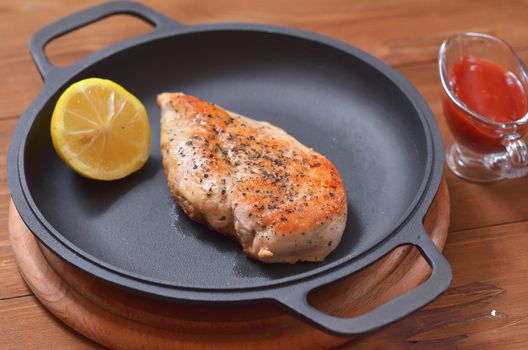 Large chicken fillet with lemon fried in a pan, next to the table there is a saucer