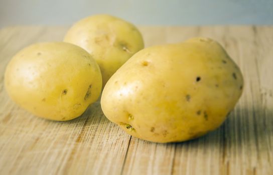 Three Raw potatoes on a wooden cutting board. Fresh organic potato.