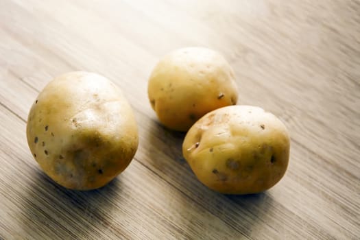Three Raw potatoes on a wooden cutting board. Fresh organic potato.