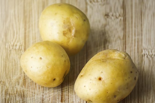 Three Raw potatoes on a wooden cutting board. Fresh organic potato.