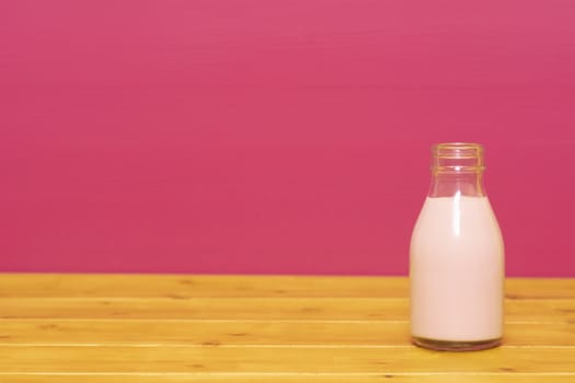 Strawberry milkshake in a one-third pint glass milk bottle, on a wooden table against a pink painted background