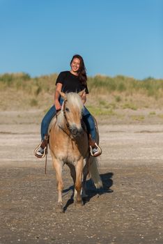 eighteen year old girl riding on a haflinger horse on the beach with the dunes as background