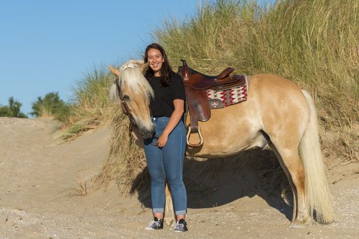 eighteen year old girl posing with her haflinger horse on the beach with the dunes as background