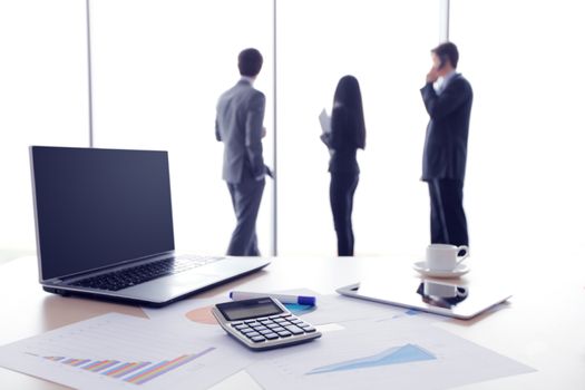 Financial documents , laptop, calculator on table , business team on background