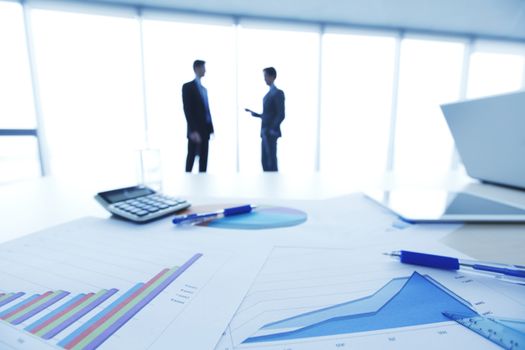 Financial documents , laptop, calculator on table , business team on background