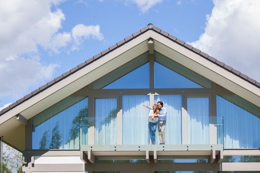 Happy couple standing on the balcony of their house and waving hands