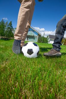 Cheerful father and son playing football on the backyard lawn near their house