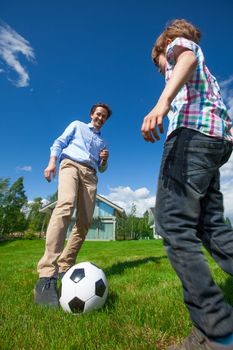 Cheerful father and son playing football on the backyard lawn near their house