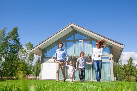 Happy family with children running on lawn near their house
