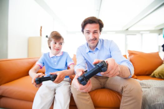 Father and son sitting on sofa in lounge playing video game