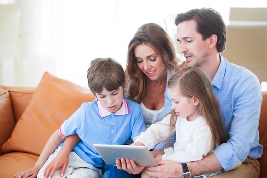 Portrait of happy family with two children sitting on sofa and using digital tablet pc