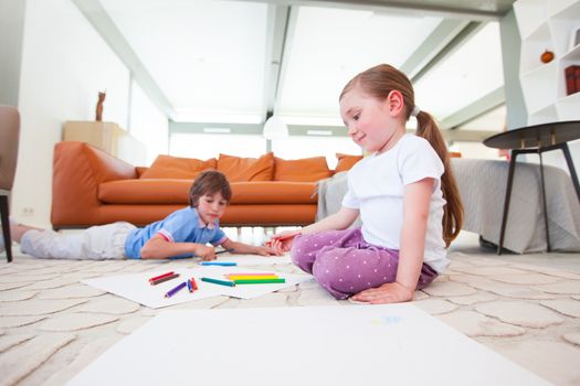 Little boy and girl drawing with color pencils on the floor playing together