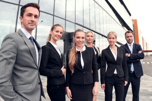 Portrait of successful business people team standing together outdoors near modern office building