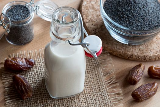 A bottle of poppy seed milk on a wooden table, with poppy seeds and dates in the background