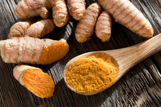 Turmeric powder on a wooden spoon, with fresh turmeric root in the background