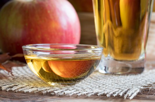 Apple cider vinegar in a glass bowl, with an apple in the background