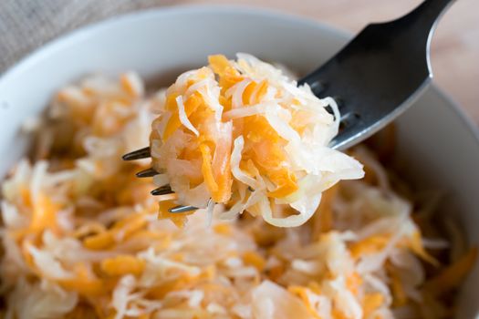 Fermented cabbage and carrots on a fork above a bowl of fermented vegetables