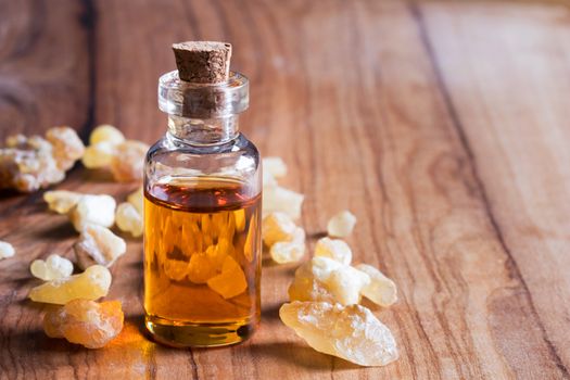 A bottle of frankincense essential oil with frankincense resin on a wooden background with copy space