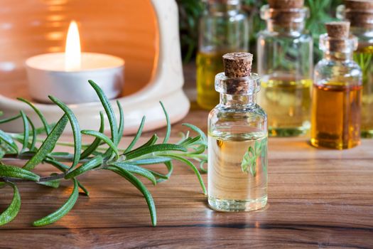 A bottle of rosemary essential oil with fresh rosemary twigs, with a candle and other bottles in the background