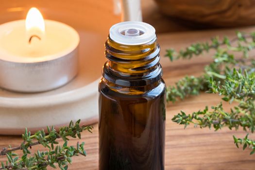 A dark bottle of thyme essential oil with fresh thyme twigs and a candle in the background