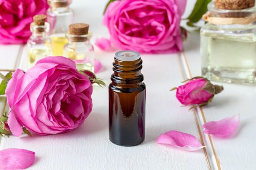 A bottle of essential oil with fresh roses on a white background