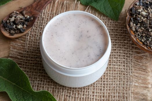 A jar of homemade comfrey ointment with fresh symphytum officinale leaves and dried root