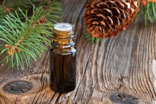 A bottle of essential oil with spruce branches on a rustic background