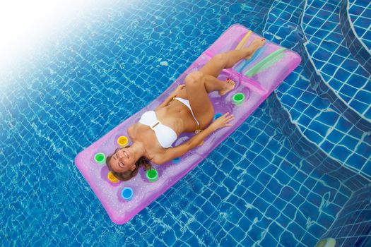 Enjoying suntan. Vacation concept. Top view of slim young woman in bikini on the pink air mattress in the swimming pool.