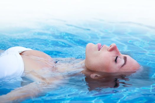 Girl in bikini relaxing floating in blue water of swimming pool