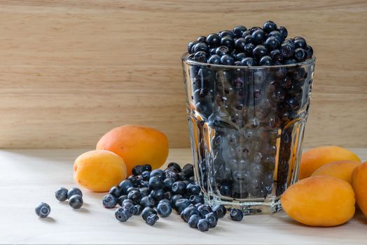 Blueberries in a glass with scattered berries and few apricot. Good addition for healthy breakfast