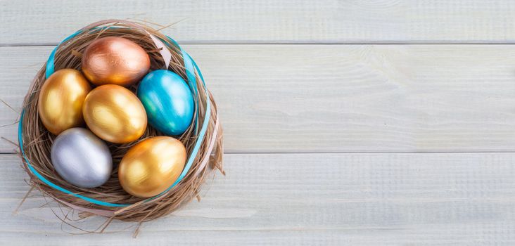 Beautiful Happy Easter holiday greeting banner with easter nest with colored eggs and decorated with ribbons over light wooden background with copy space for text