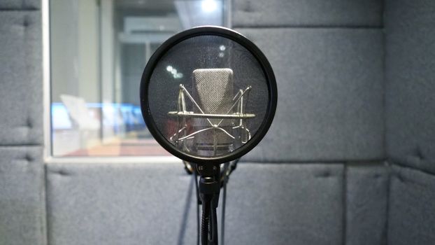 Studio microphone or mic for recording for vocal singer or commercial announcer with shock mount and pop filter on professional tripod in acoustic foam room for best sound and mix process