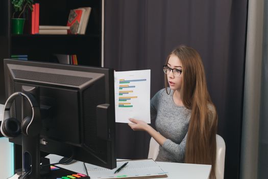 business woman in glasses in the office shows graphics online through the computer