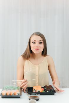 young beautiful girl eats sushi rolls with chopsticks on a white background portrait