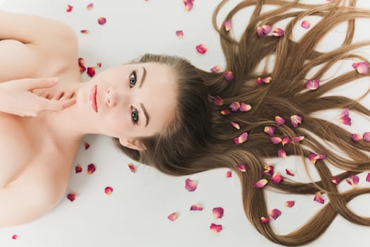 young beautiful healthy girl lying on a white background with long hair and flower petals